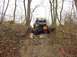 1992 Ford Bronco - A modified off-road vehicle navigates a challenging, muddy, and rocky incline through a wooded area.