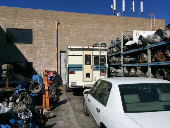 White motorhome with teal and cream stripes parked next to a rack of transmissions