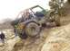 1992 Ford Bronco - Modified off-road vehicle navigates a rocky, muddy incline with a spare tire mounted on the back.