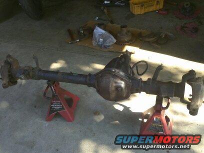 Differential axle assembly on red jack stands, with tools and parts in background
