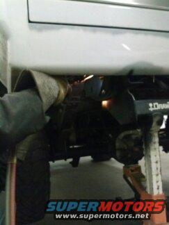 White vehicle frame on jack stands with a person welding underneath