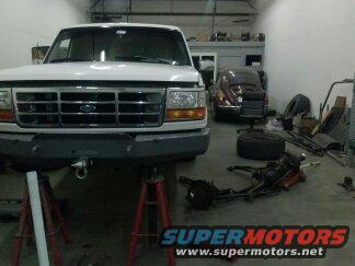 White Ford truck on jack stands, front view. Grille has horizontal bars and rectangular headlights