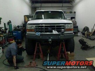 Front view of a white 1995 Ford Bronco on jack stands in a garage with a person working on it