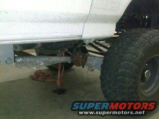 close-up of a white vehicle's undercarriage, showing suspension, a tire, and part of the body