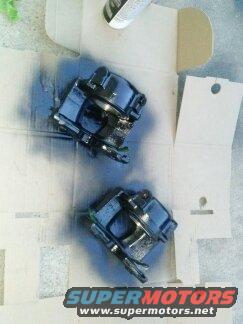 two black brake calipers on cardboard, one being sprayed with black paint