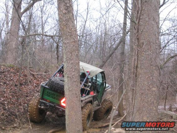 Off-road buggy with spare tire on back, driving on muddy trail through trees