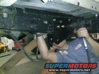 Undercarriage of vehicle with mechanic working on suspension. SuperMotors.net logo