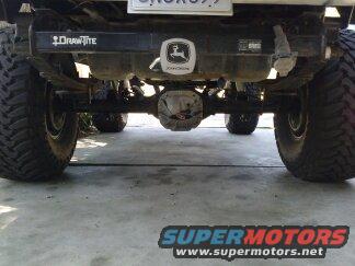 Rear view of a truck's axle, suspension, and large tires. Draw-Tite hitch with John Deere logo visible