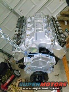Polished Ford V8 engine assembly with intake manifold and valve covers. Supermotors.net logo visible
