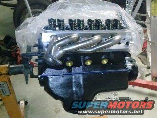 Ford V8 engine block with aluminum heads and chrome headers, covered in plastic