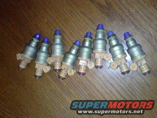 Eight fuel injectors with blue tops on a wooden surface