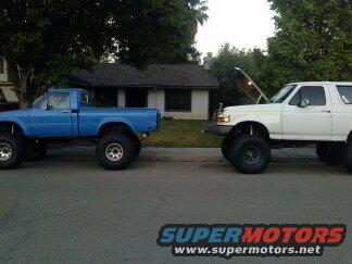 White Ford Bronco with hood up, parked next to a blue pickup truck on a residential street