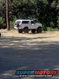 White lifted SUV parked on dry grass with trees in background