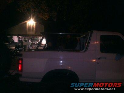 White SUV with a roll cage, side view, dark conditions, visible taillight and door handle