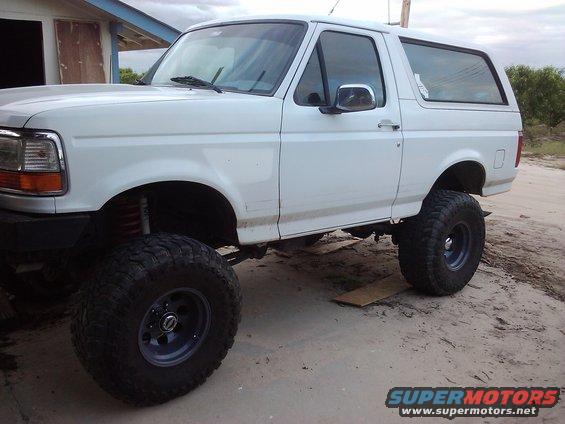 White 1995 Ford Bronco with lifted suspension and large off-road tires parked on dirt