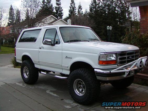 White 1995 Ford Bronco with large tires and a brush guard, parked on a driveway
