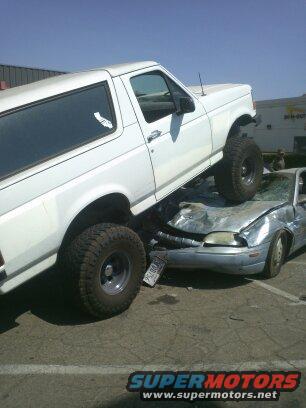 White 1995 Ford Bronco on top of a crushed silver sedan
