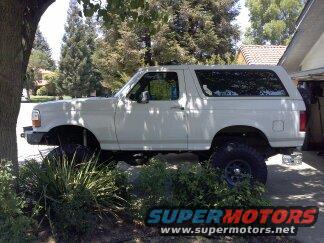 White 1995 Ford Bronco parked on rocks next to a tree and garage