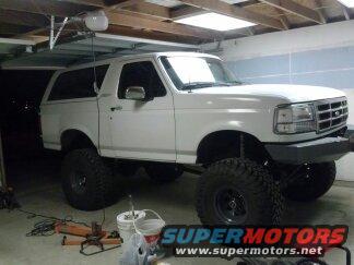 Lifted white 1995 Ford Bronco parked inside a garage with large off-road tires