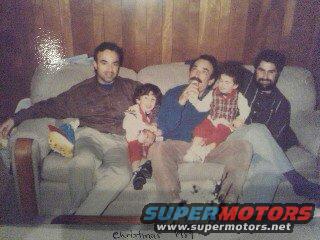 Three men and two children sit on a couch, with a toy on the left