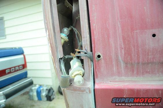 close-up of a red vehicle's exposed tail light wiring and bulbs, with a blue and white Ford truck in the background