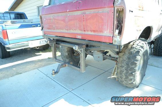 Red Ford Bronco rear with custom hitch, large off-road tires, and a blue pickup truck behind it