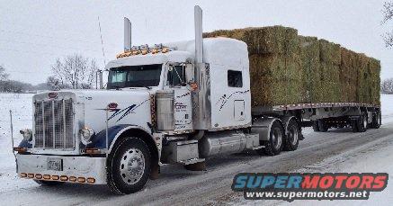 2003 Peterbilt 379 semi-truck with a load of hay bales on a flatbed trailer, driving on a snowy road