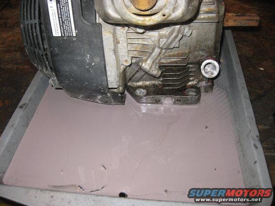 engine block with oil drain plug removed, draining into a pan