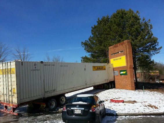 Tractor-trailer partially off a ramp with a car parked nearby in a snowy lot
