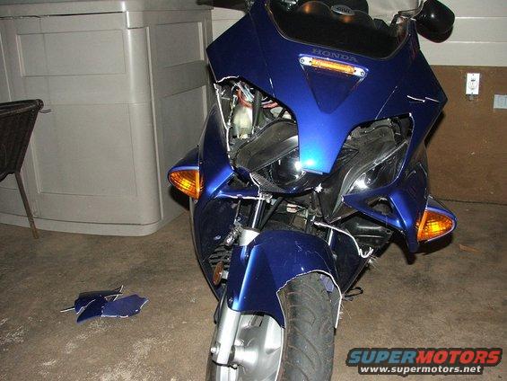 Blue motorcycle with damaged front fairing and loose body panels on the ground