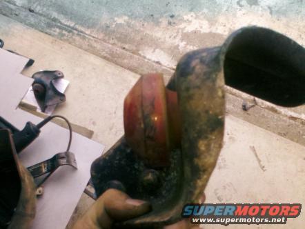 Rusty vehicle part with red lens held in hand, Supermotors.net logo visible