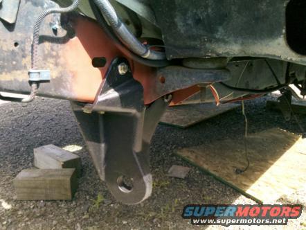 Black tow hitch bracket attached to red and black vehicle frame, with wooden blocks on the ground