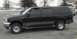 2001 Ford Excursion - This black Ford Excursion is parked in a lot with snow on the ground and trees in the background.