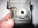 2003 Ford Escort - A hand holds a metal automotive part with a central hole, possibly for a hose or sensor.