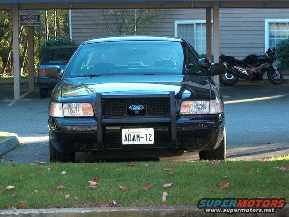 2001 Ford Crown Victoria with push bar and license plate ADAM-12 parked under a carport