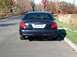 2001 Ford Crown Victoria - The rear of a dark blue 2001 Ford Crown Victoria is shown from a low angle, parked on a road with trees in the background.