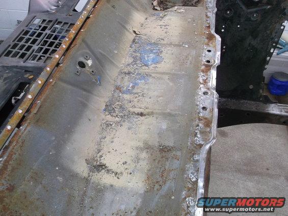Close-up of a rusty, dirty vehicle floor pan with some blue paint remnants