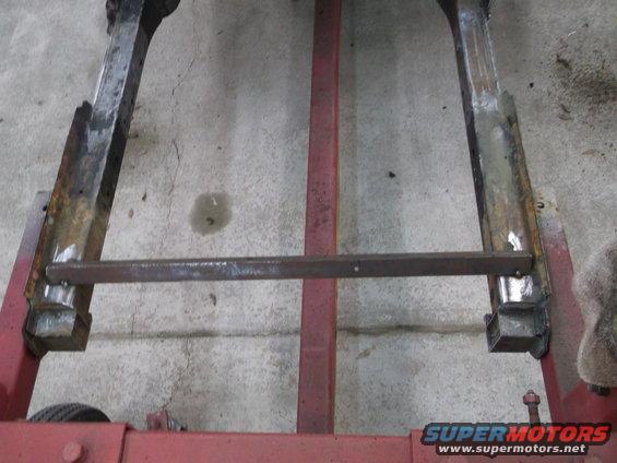 Close-up of rusted metal frame pieces on a red stand, with a horizontal bar connecting them