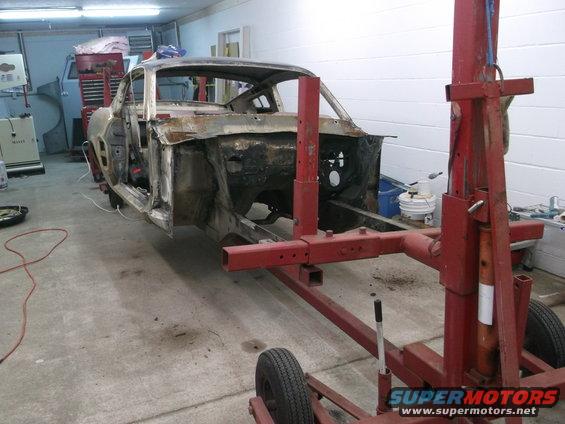 1967 Ford Mustang body shell on a red frame machine, showing extensive rust and damage