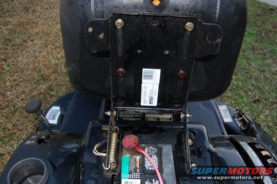 Close-up of a lawn tractor's battery and seat mounting bracket. Visible labels include MTD
