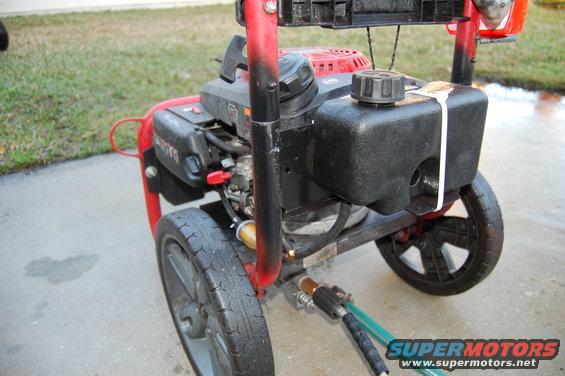 Red pressure washer with black gas tank and wheels, connected to a green hose
