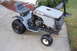 2010 Kawasaki BAYOU 220 - This Craftsman riding mower is parked on a concrete driveway with grass and bushes in the background.