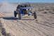 1996 Ford Bronco - A blue off-road buggy kicks up dust as it jumps over a dirt track in a desert landscape.