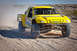 1996 Ford Bronco - Off-road race truck with drivers in helmets navigates a dusty desert course.