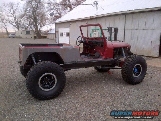 1985 Jeep CJ7 body, red with gray fenders, on large off-road tires, parked outside a barn
