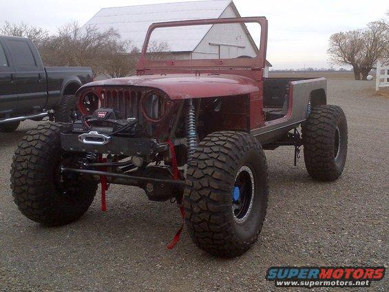 Red Jeep CJ-series body with large off-road tires and a winch, parked next to a black pickup truck