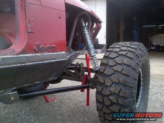 Red Jeep body with custom suspension and large off-road tire. Some body panels removed