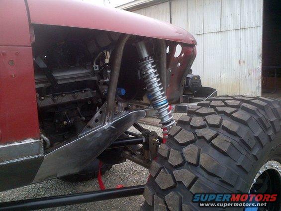Red off-road vehicle with exposed engine, large tire, and custom suspension
