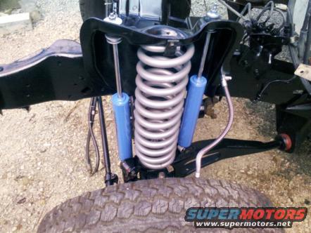 Front suspension with large coil spring and blue shock absorber mounted to black frame. Tire visible below