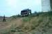 1979 Ford Bronco - A person watches a 1979 Ford Bronco ascend a steep, grassy incline near a large concrete pillar.